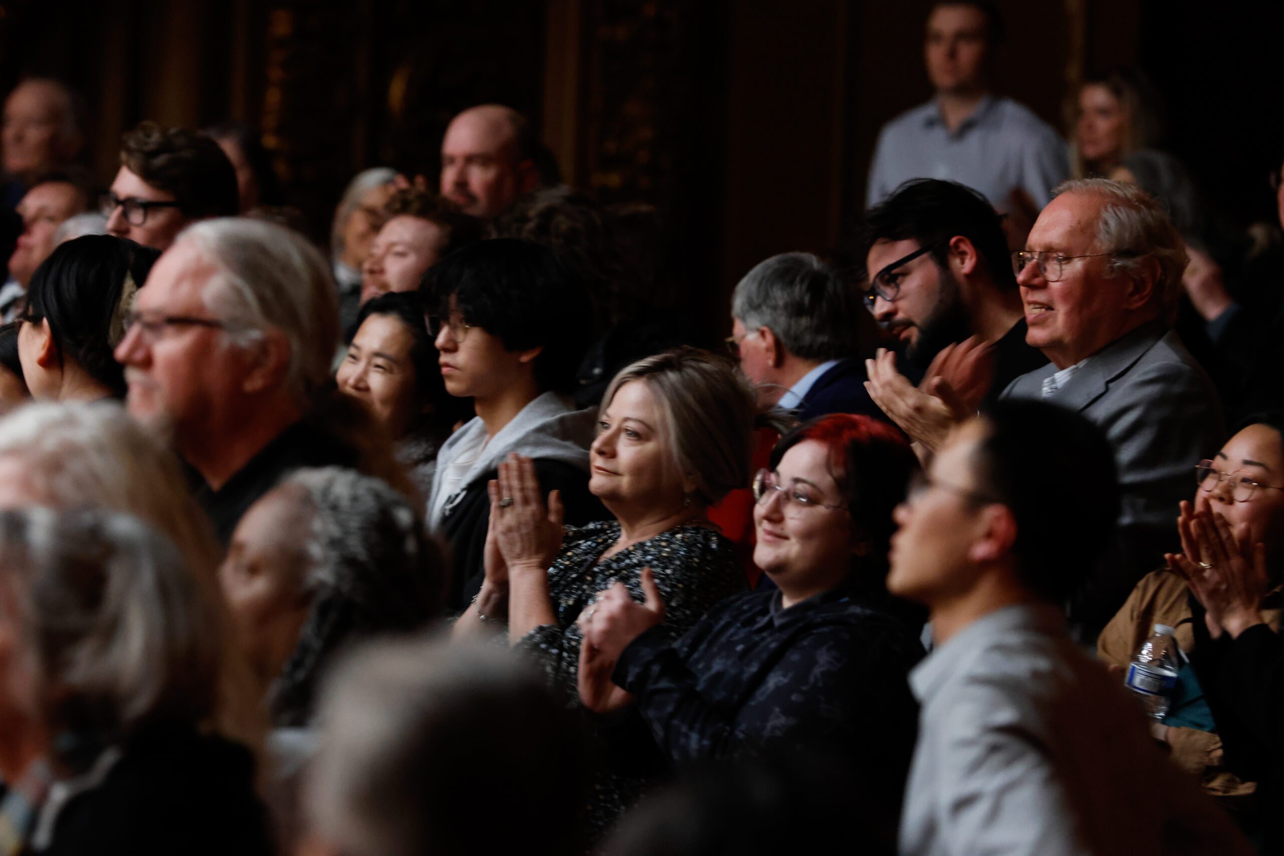 Audience members are clapping and appear to be attending an event, possibly a concert or performance.